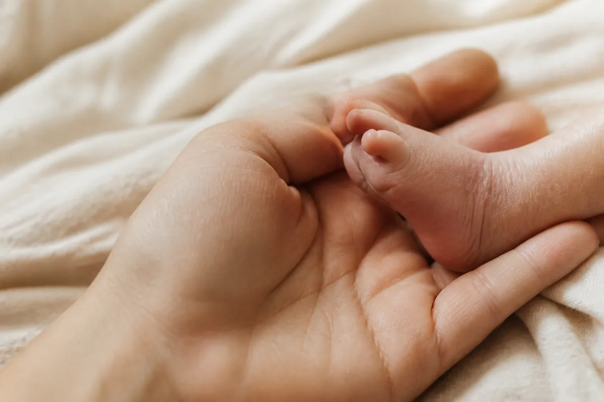 Main d’adulte tenant le pied nu d’un nourrisson sur un drap clair